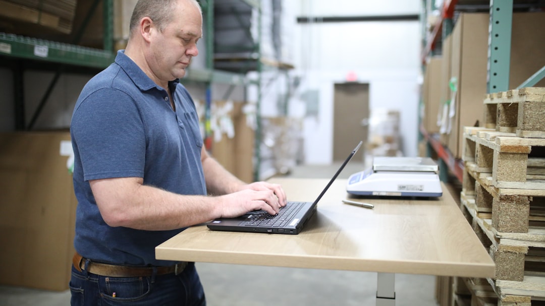 A small business owner checks a laptop while standing near warehouse shelving