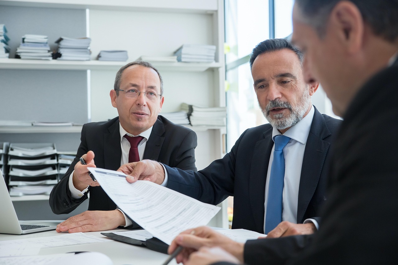 Coworkers gather around a laptop and printed documents during a team meeting