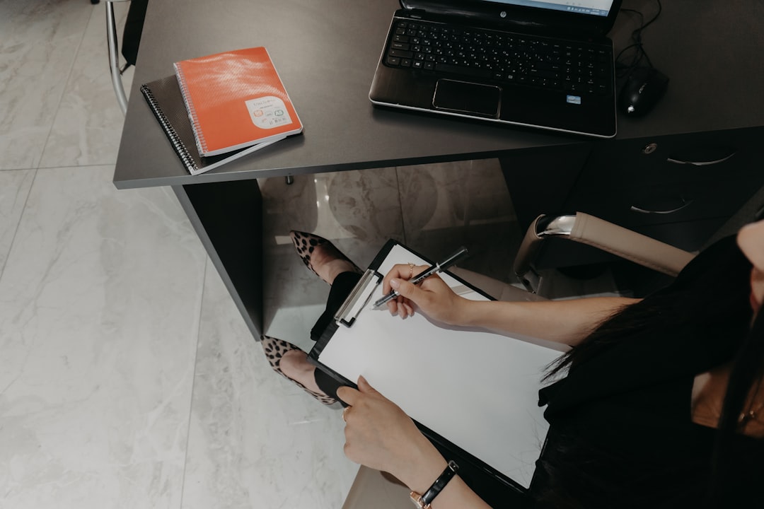 Person writing on a clipboard checklist at a desk beside a laptop