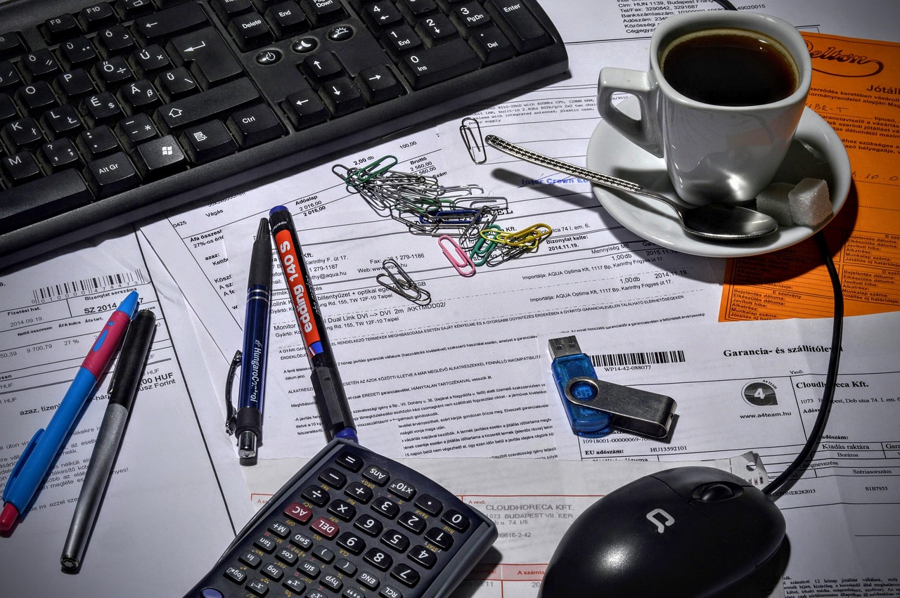 Small business bookkeeper using a calculator with invoices and paperwork on a desk