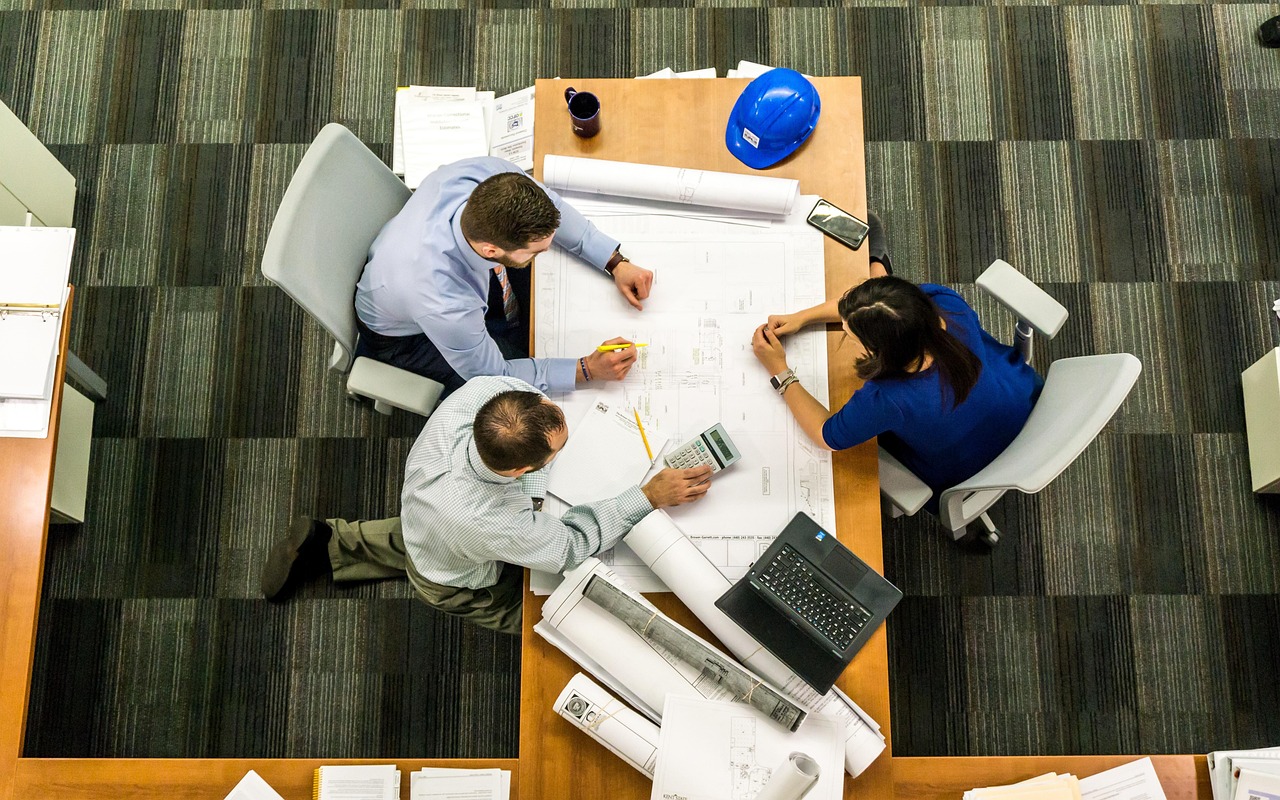 A small team gathers around an office table reviewing documents and plans together