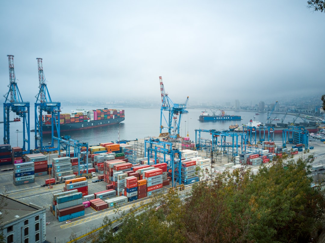 Stacked shipping containers at a busy cargo port, representing cross-border trade and supply chains