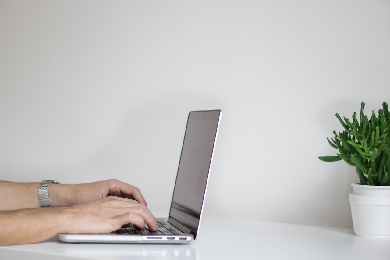 Hands typing on a laptop keyboard at a home office workspace