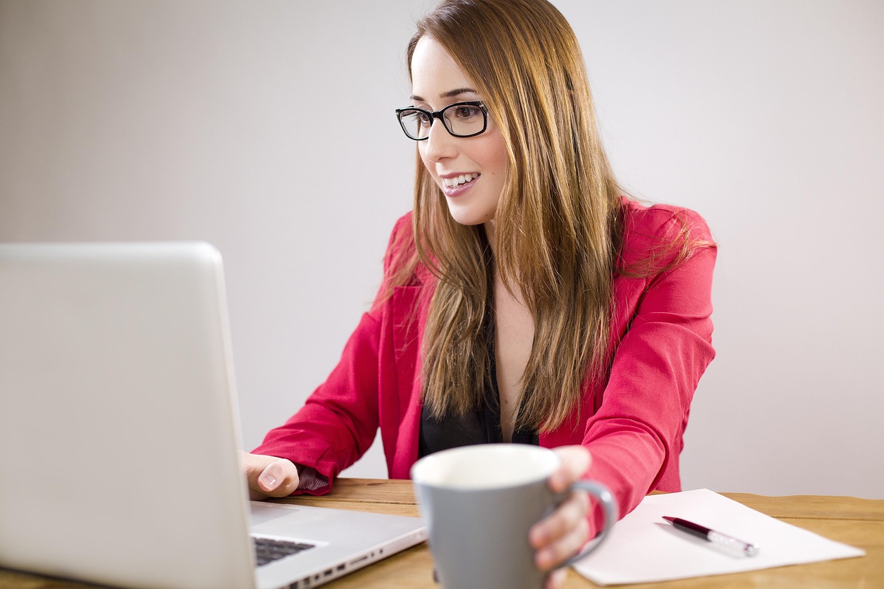 Small business owner working at a laptop on office paperwork, smiling at her desk