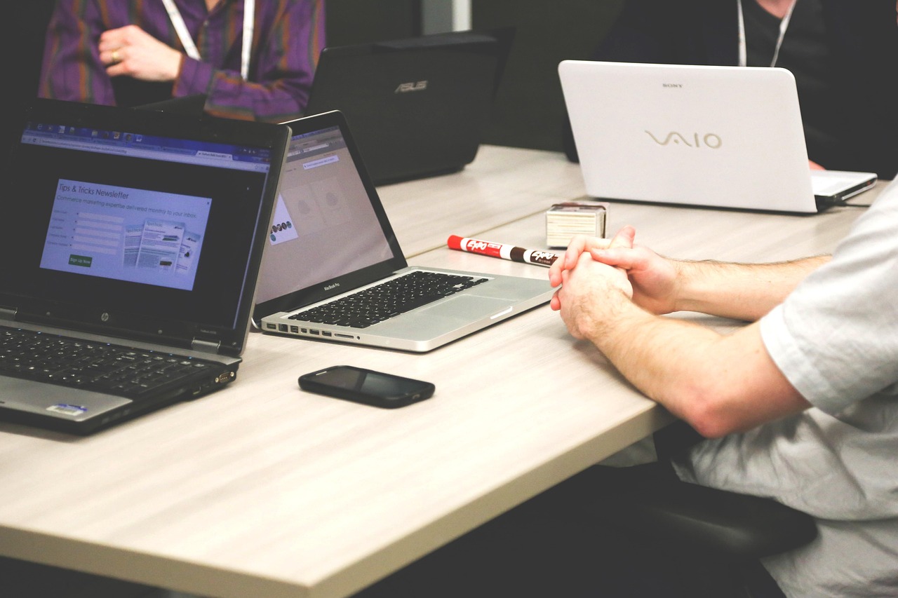 Colleagues from two companies meeting around a table with laptops, discussing a joint bid